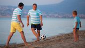 Una familia disfruta jugando al futbol en la playa.
