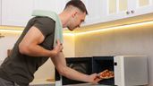 Imagen representativa de un joven metiendo una pizza en el microondas