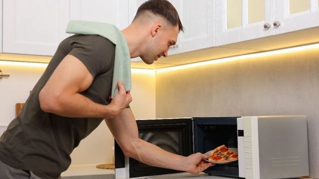 Imagen representativa de un joven metiendo una pizza en el microondas