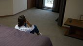 Una joven sentada en el sueldo, junto a la cama