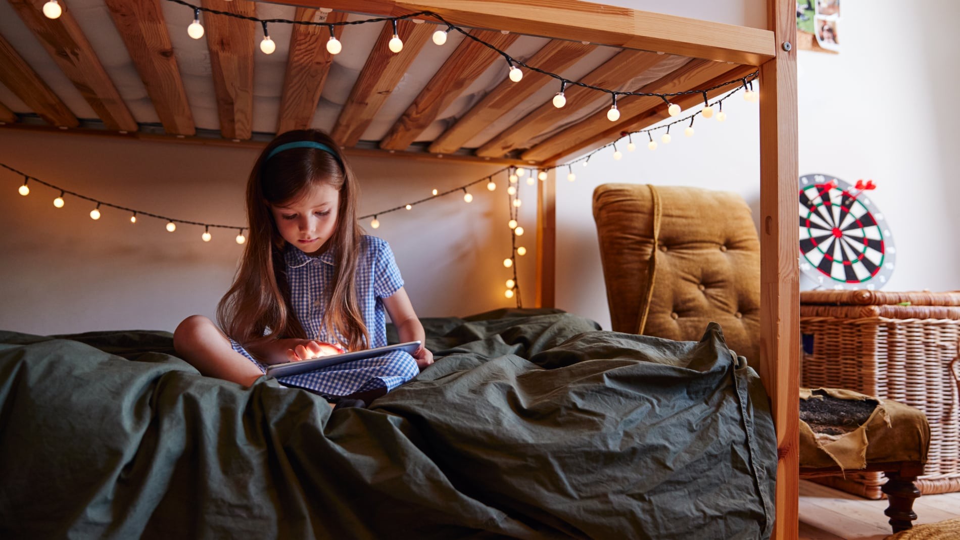 Chica joven sentada en la cama en casa decorada con luces de hadas