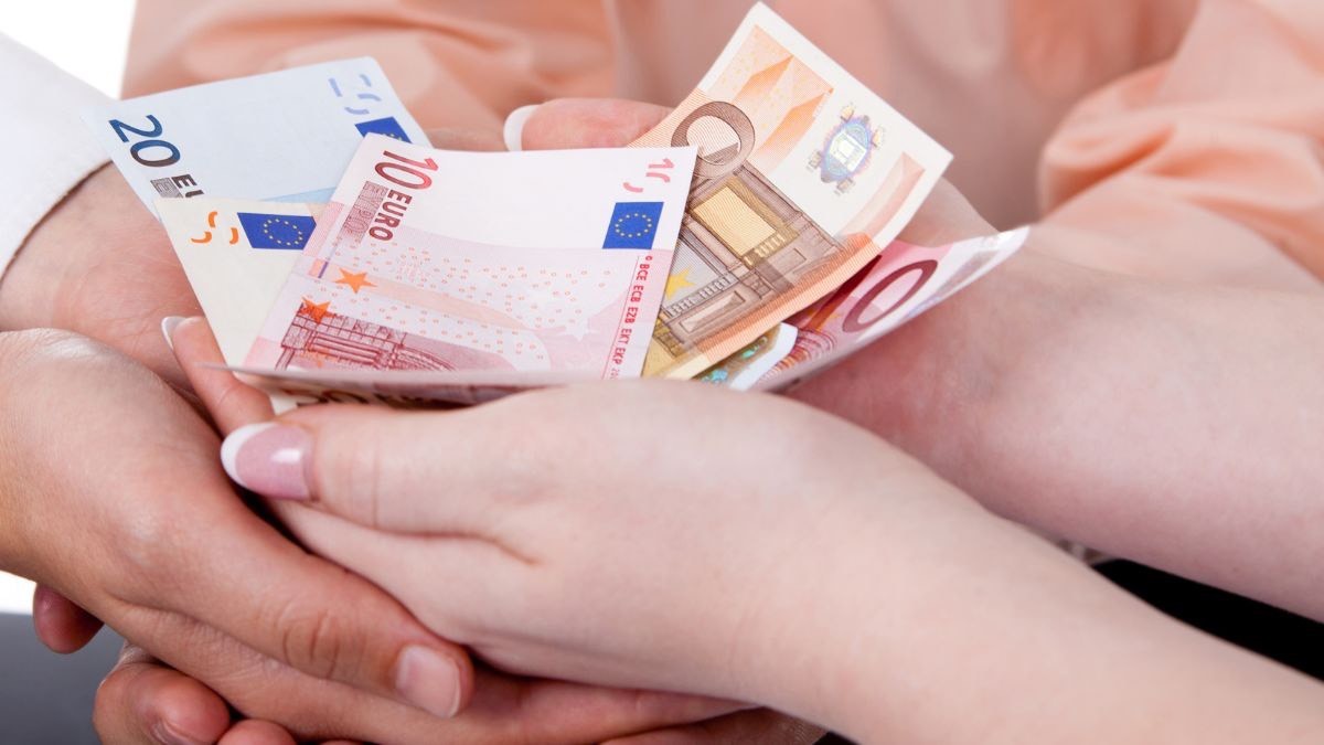 Manos de una familia con euros en la mano. Ingreso Mínimo Vital: ¿tiene paga extra este verano?
