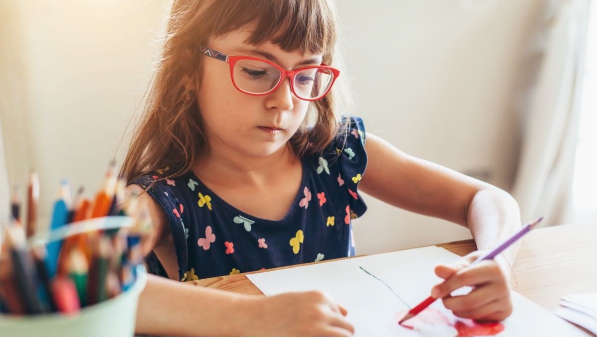 niña con gafas dibujando Las familias podrán disfrutar de una bonificación que aplicará en las ópticas al momento de comprar o renovar los lentes graduados.
