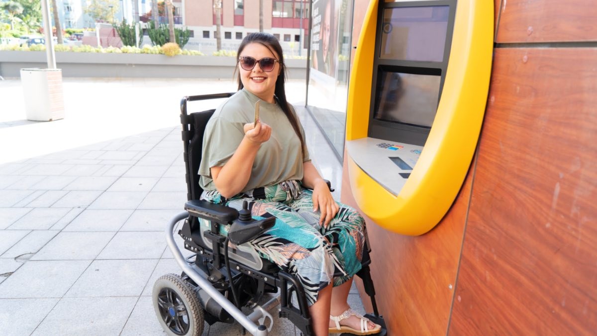 La paga extra de la Seguridad Social que puedes cobrar en junio si tienes una incapacidad permanente persona en silla de ruedas sacando dinero del cajero automático