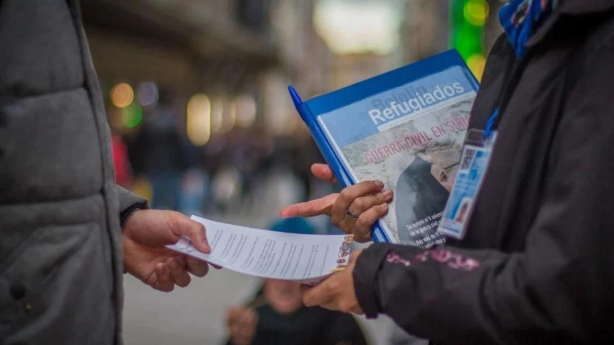 Un captador de socios de una ONG entrega un documento a un viandante.