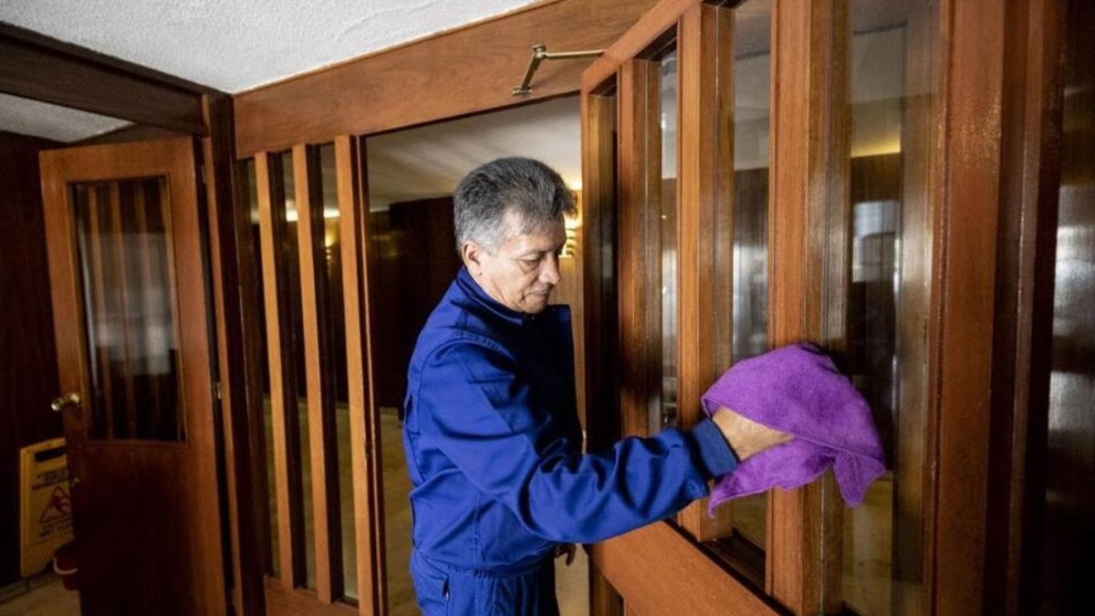 Se necesitan conserjes para comunidades de vecinos: sin experiencia, estudios mínimos y salario de 1.400€ conserje de comunidad de vecinos limpiando con un trapo las ventanas